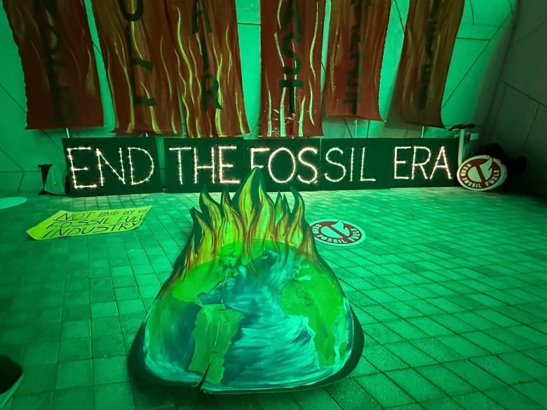 Posters sit on the ground and against a wall. One poster shows a planet on fire and another reads 'end the fossil era.'