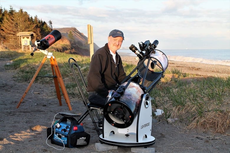 A man is shown by a beach with a large telescope.