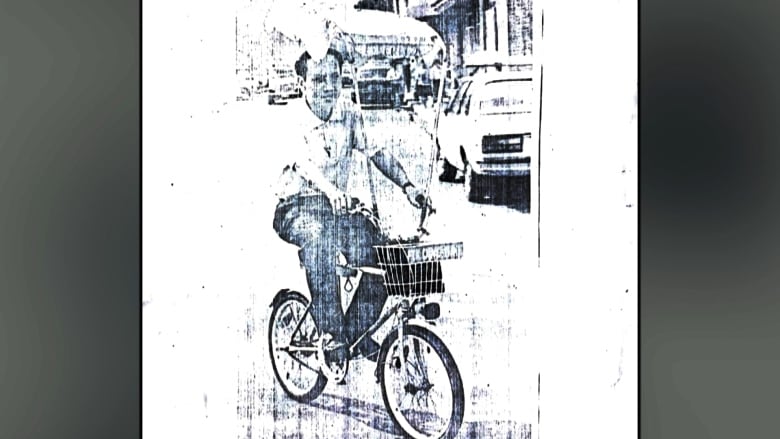 An East Asian man rides a bicycle with a parasol on it in a black-and-white, aged photo.