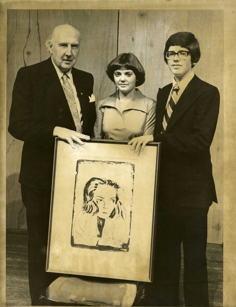 Black and white photo shows three people posting with a painting of a woman