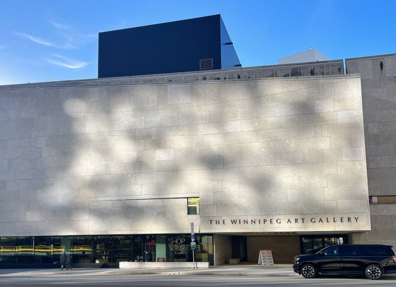 The exterior of a building, seen from across the street with the sun beaming on its stone wall. The words Winnipeg Art Gallery are seen on the outside.