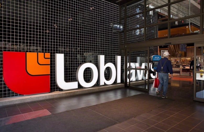 A man carrying a shopping bag walks past a huge sign bearing the words "Loblaw's" on his way into a grocery store.