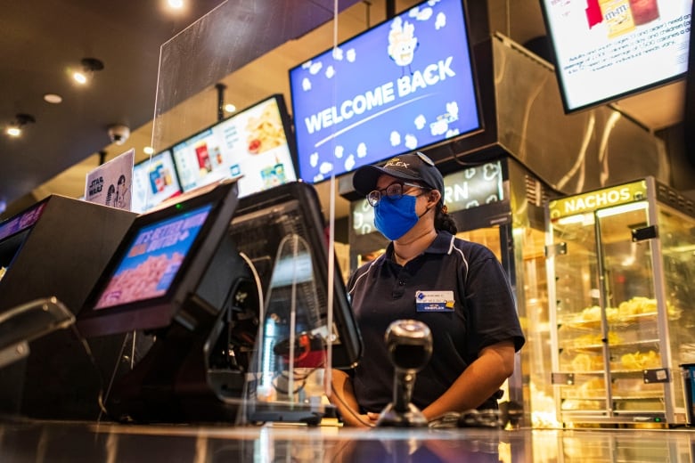 A person is scene waiting to serve customers behind the concession stand at a movie theatre.
