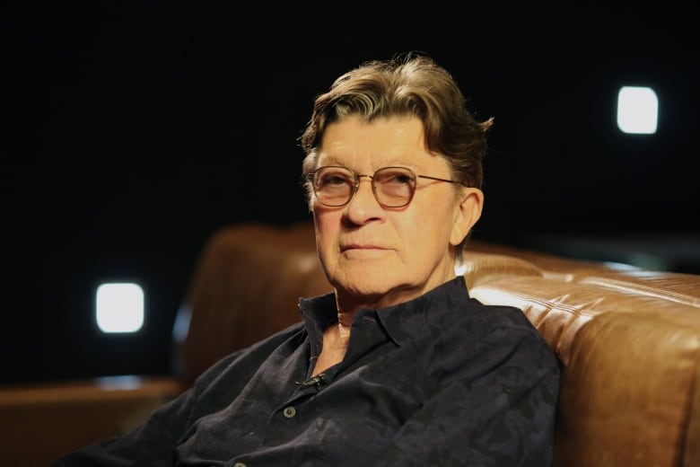 A man wearing glasses sits on a couch.