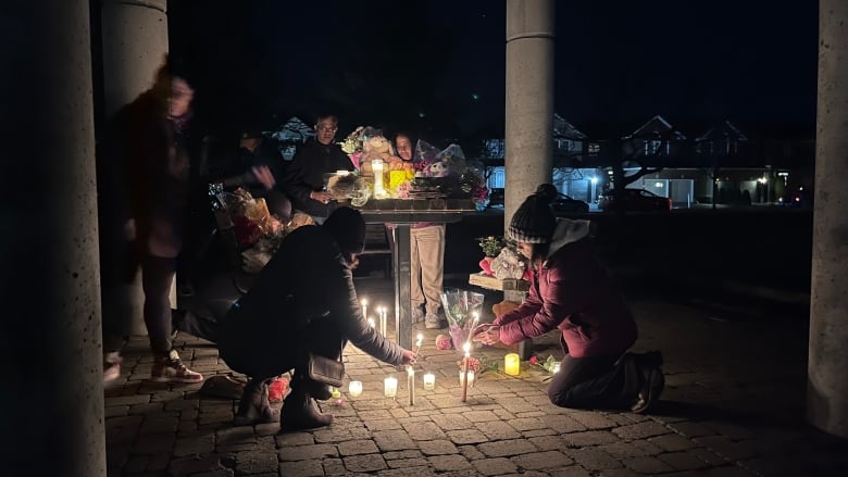 A crowd of people lay flowers and light candles.