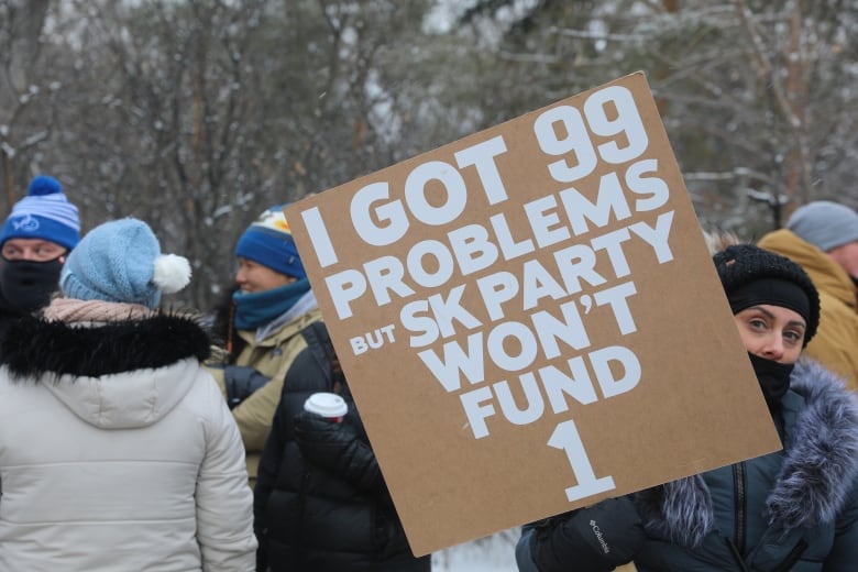 A woman holds a sign with the phrase "I got 99 problems but SK Party won't fund 1."