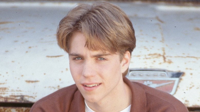 Jonathan Brandis posing in front of a rusty car