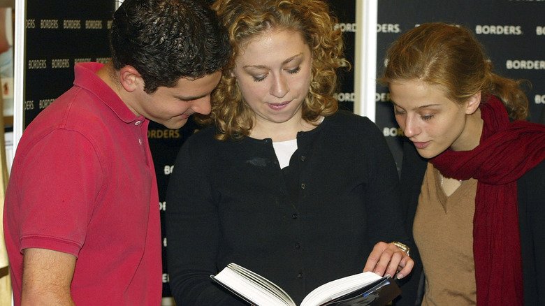 Chelsea Clinton reading a book as two others look in