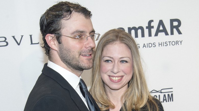 Marc Mezvinsky and Chelsea Clinton smiling on step-and-repeat