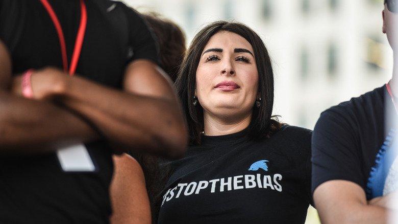 Laura Loomer stands behind men with folded arms