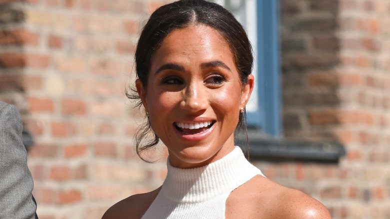 Meghan Markle smiling with bricks behind her