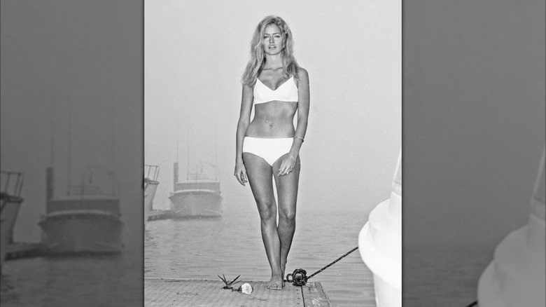 Farrah Fawcett wearing a white bikini on a dock with a boat behind her