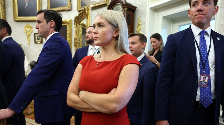 Karoline Leavitt standing with her arms folded in the Oval Office.
