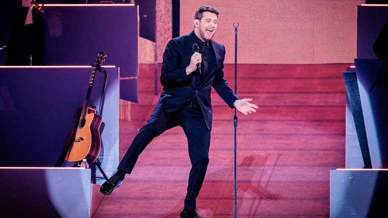Michael Bublé wearing a black suit and holding his leg out while singing into a microphone