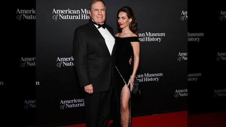 When Two Worlds Walk the Red Carpet — Bill Belichick and Jordon Hudson’s Unmistakable Contrast 129 Bill Belichick wearing a tux on the red carpet with Jordon Hudson, who is wearing a black dress with a slit
