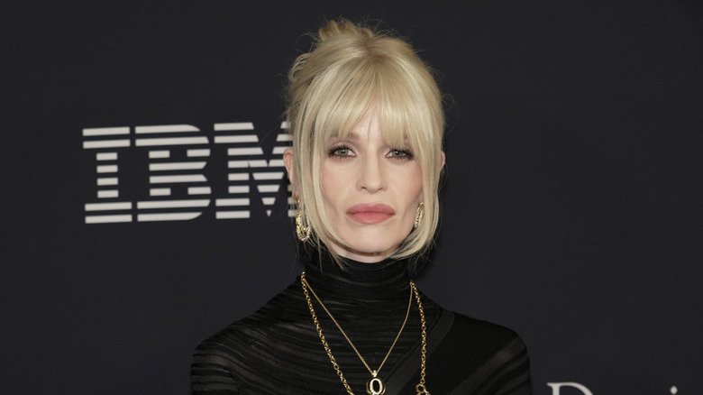 Kelly Osbourne posing at an event in a black turtleneck with gold jewelry