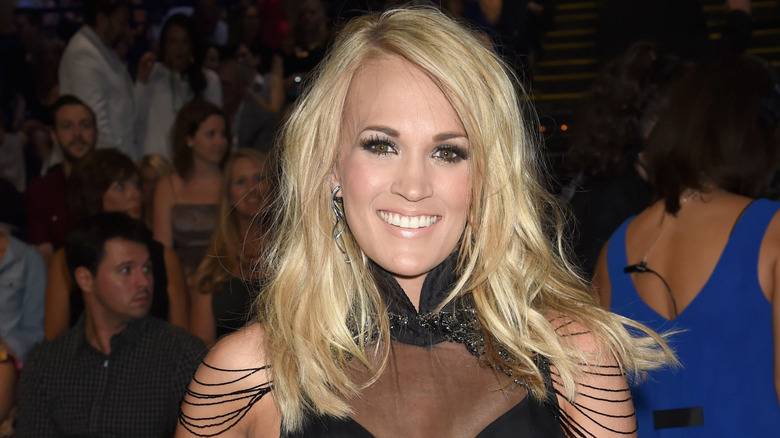 Carrie Underwood Original Lips: A Look Back Before the Big Change 142 Carrie Underwood smiling in glam black outfit with her hair styled in messy waves with a deep side part.