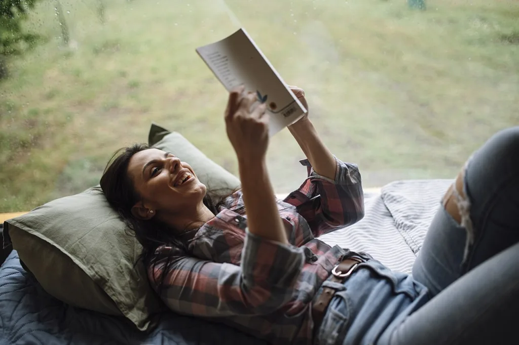 Woman reading a book while lying on a bed by a window