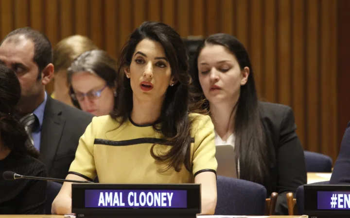 Amal Clooney speaking at a United Nations event in a tailored yellow dress