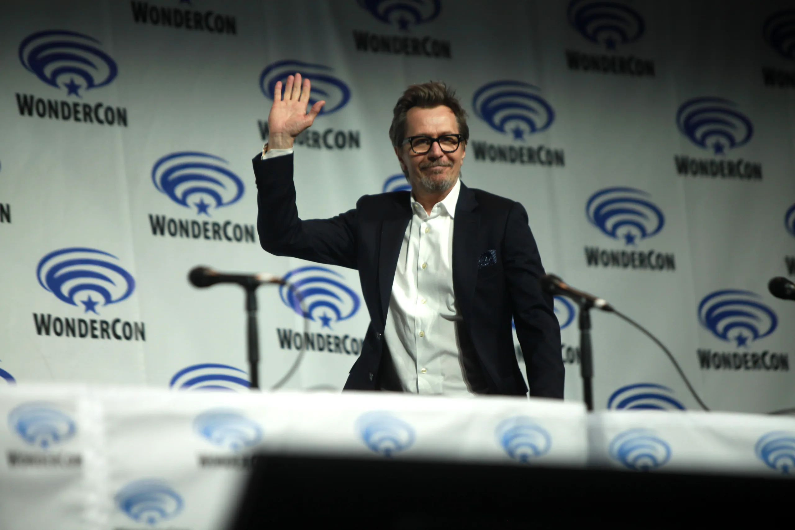 Open the featured image for Gary Oldman James Bond Claim Fuels Jack Lowden Casting Talk Gary Oldman waving at a WonderCon panel in Anaheim in 2014