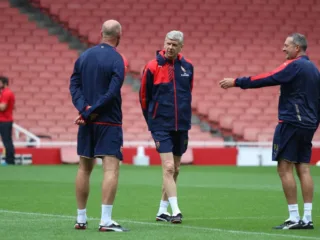 Arsène Wenger standing with Arsenal coaches on the Emirates Stadium pitch in 2015