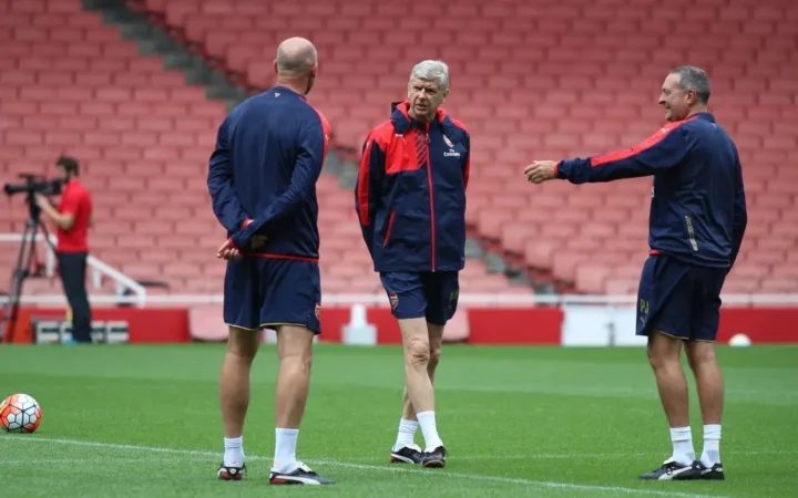 Arsène Wenger standing with Arsenal coaches on the Emirates Stadium pitch in 2015