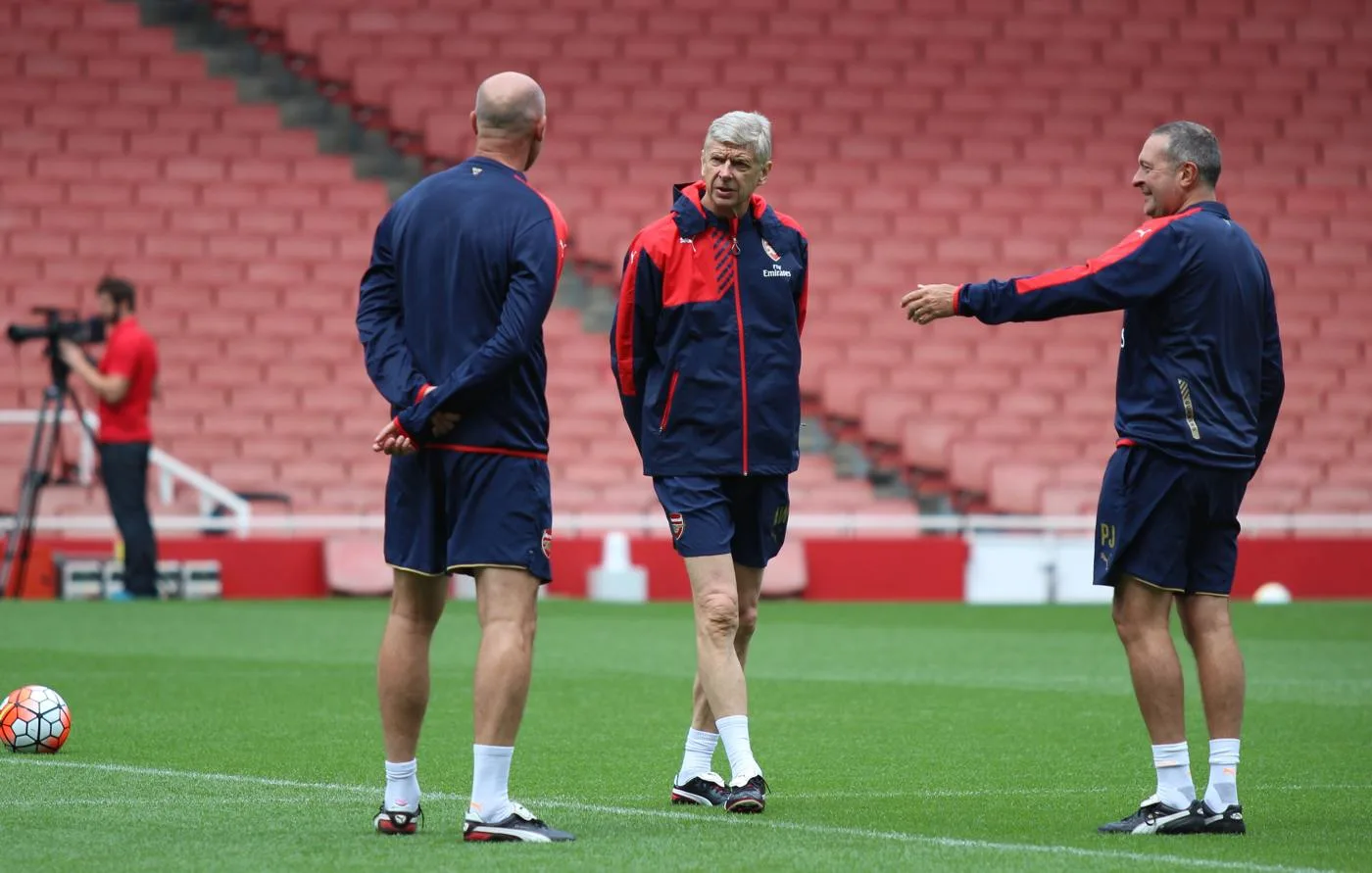 Arsène Wenger standing with Arsenal coaches on the Emirates Stadium pitch in 2015