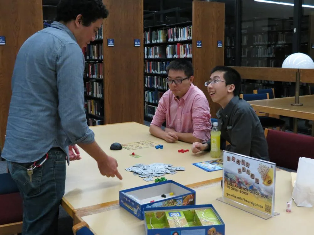 A player explaining a board game to two people at a library table