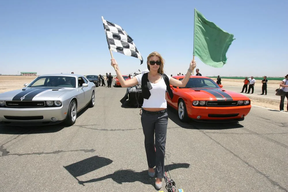 Carmen Electra holds flags between two Dodge Challenger cars at a 2008 promotional appearance