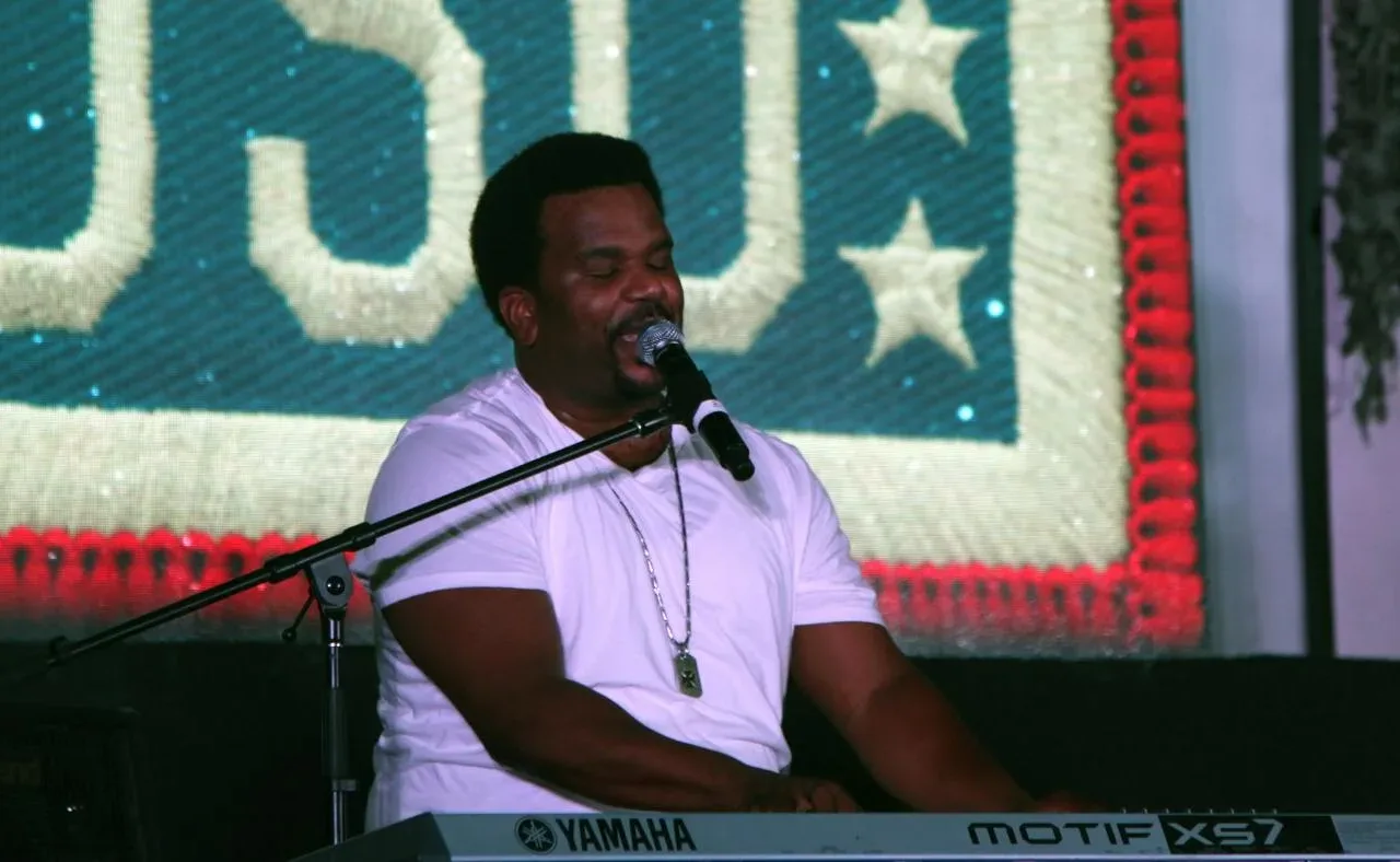 Craig Robinson sings into a microphone while playing a keyboard at a 2014 USO performance.