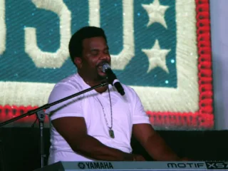 Craig Robinson sings into a microphone while playing a keyboard at a 2014 USO performance.