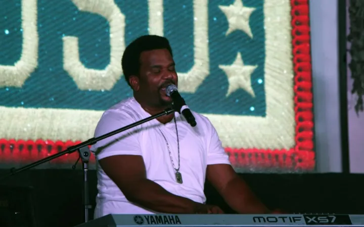 Craig Robinson sings into a microphone while playing a keyboard at a 2014 USO performance.