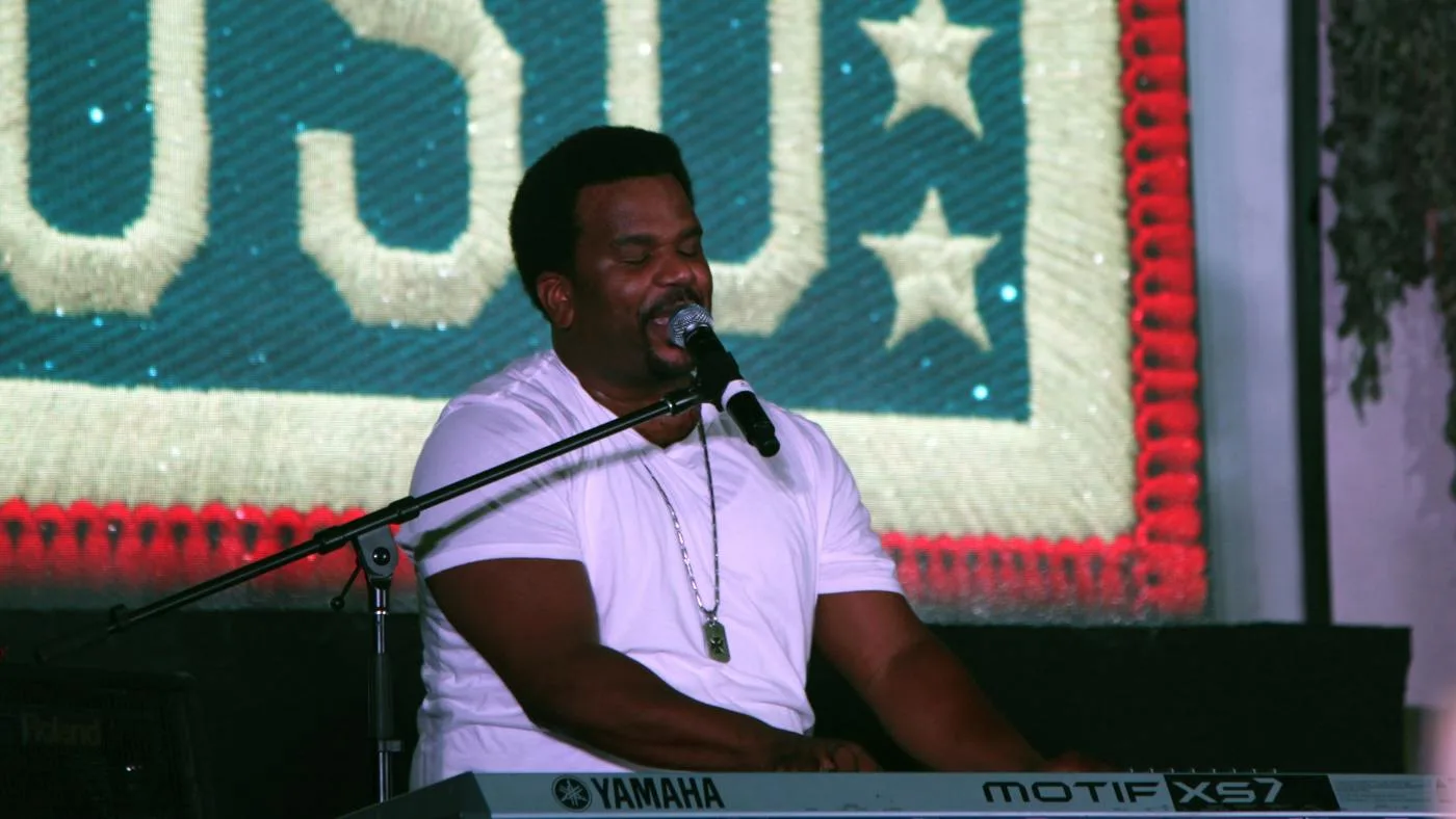 Open the featured image for Craig Robinson at 55: Music, Comedy and a Familiar Voice Craig Robinson sings into a microphone while playing a keyboard at a 2014 USO performance.