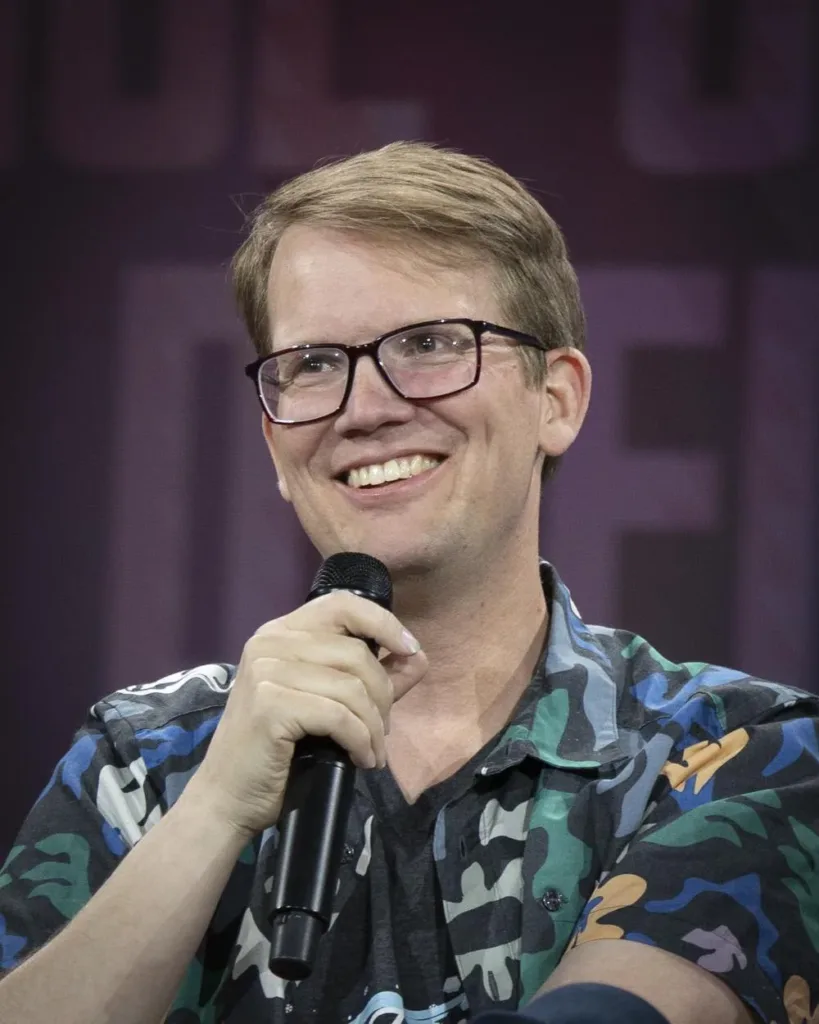 Portrait of Hank Green holding a microphone at Open Sauce in July 2026