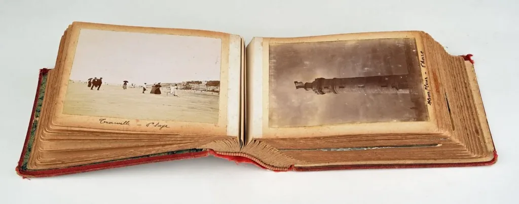 An open early twentieth-century photo album with handwritten place captions below mounted prints