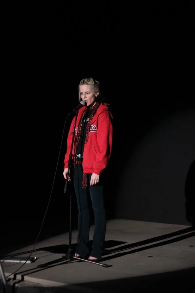 Maria Bamford in a red jacket performing at a standing microphone in June 2009