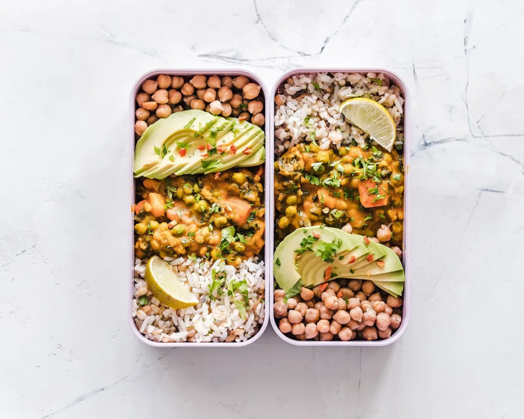 Two food containers holding prepared grains, vegetables, chickpeas and avocado