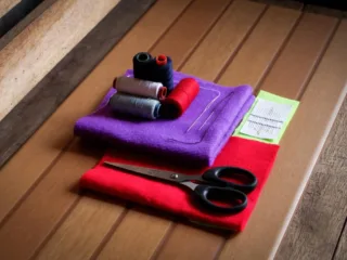 Scissors, thread and hand-sewing needles arranged on colourful fabric on a wooden table