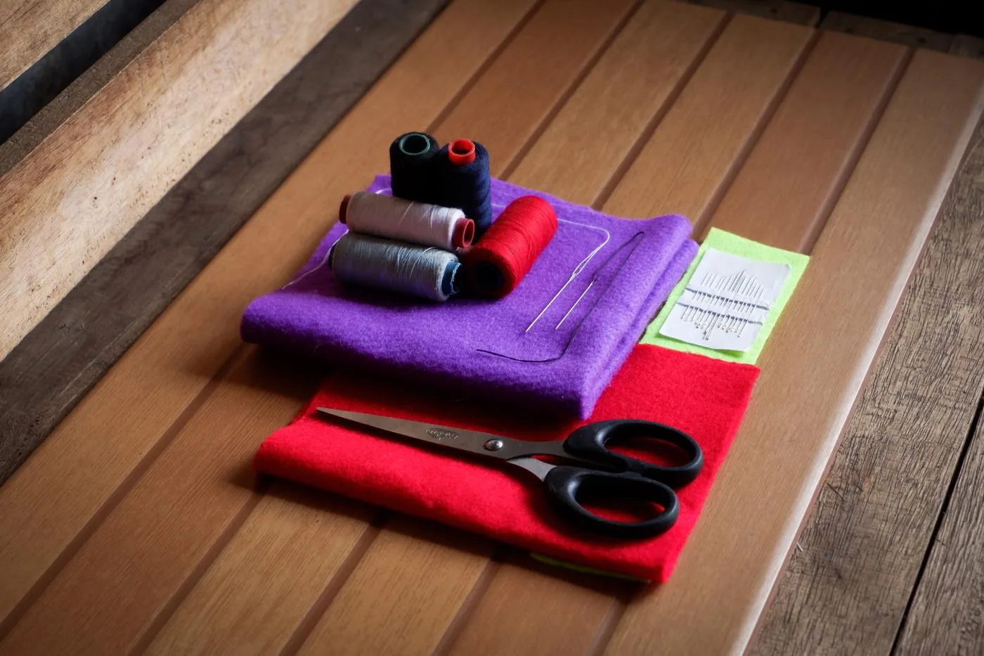 Open the featured image for Building a Mending Kit: Small Tools for Everyday Clothing Repairs Scissors, thread and hand-sewing needles arranged on colourful fabric on a wooden table