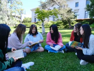 A group of young adults reading and discussing books together on a lawn