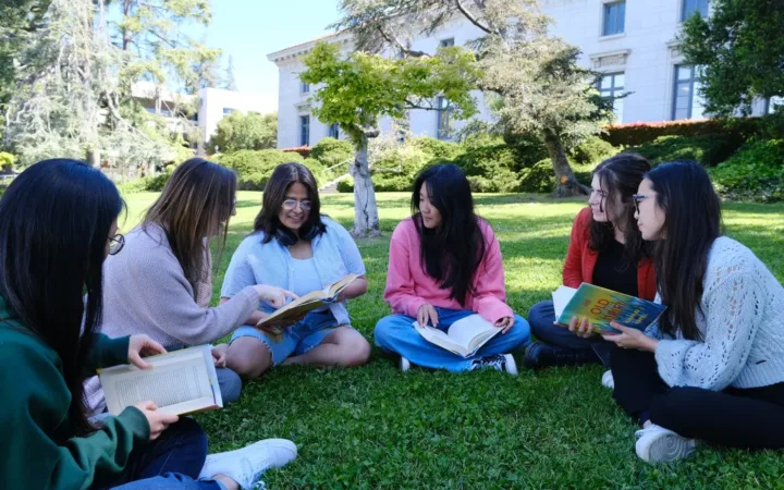 A group of young adults reading and discussing books together on a lawn