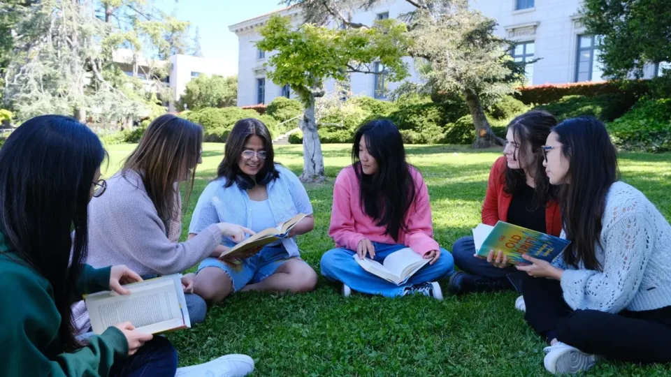 A group of young adults reading and discussing books together on a lawn