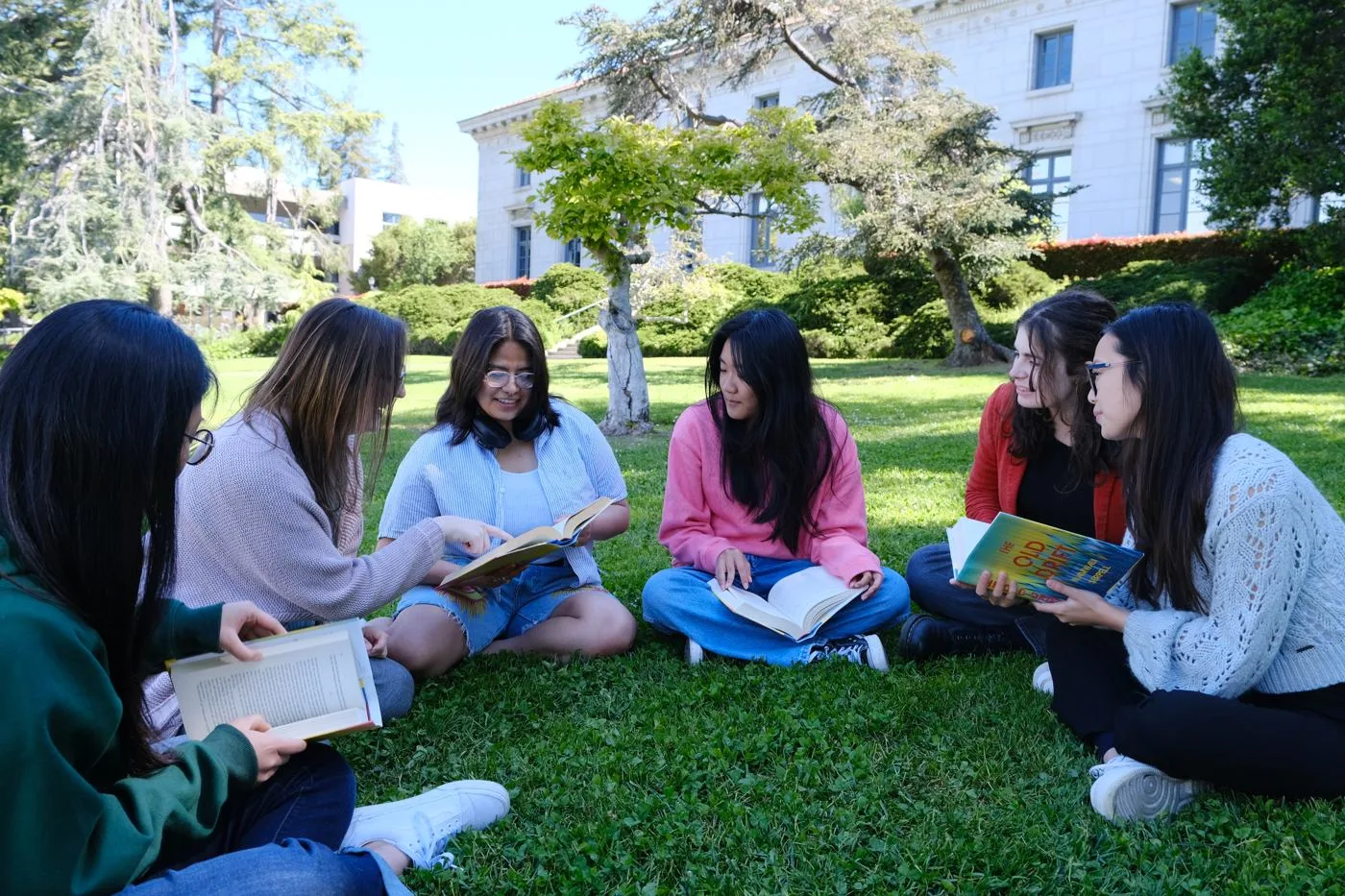 A group of young adults reading and discussing books together on a lawn