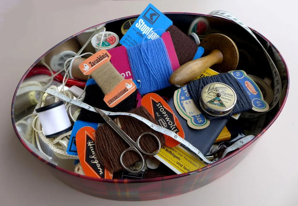 Thread, scissors, measuring tape and darning tools stored together in an open biscuit tin