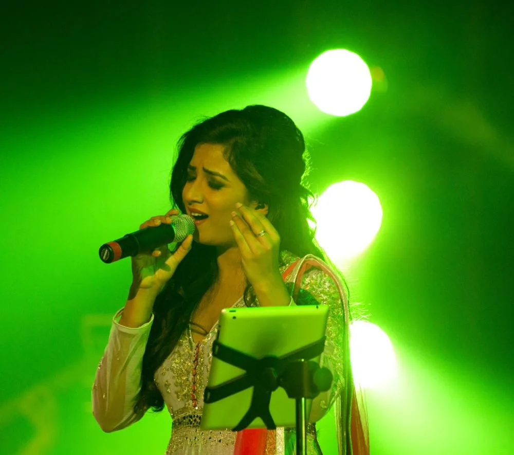 Shreya Ghoshal singing into a microphone at a concert in 2015