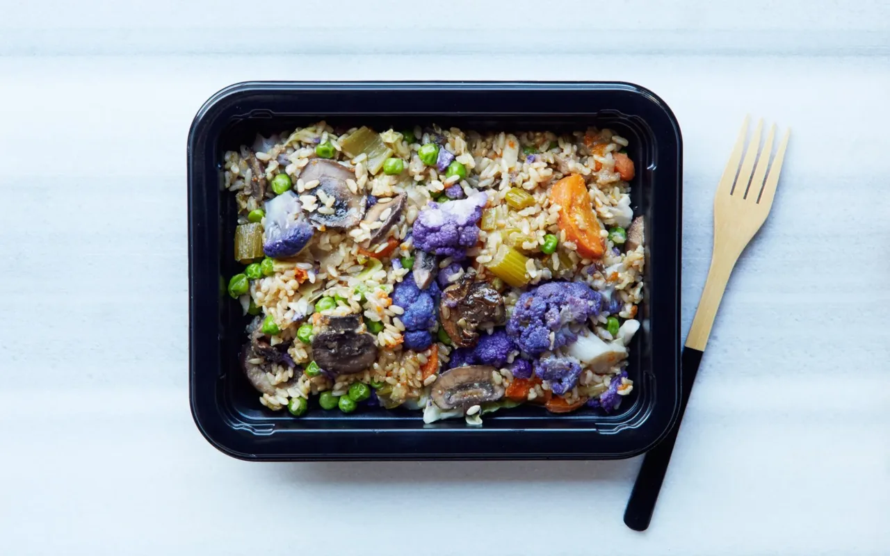 Prepared grain and vegetable meal in a food container beside a fork