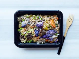 Prepared grain and vegetable meal in a food container beside a fork