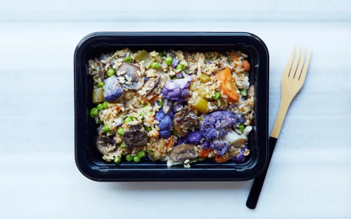 Prepared grain and vegetable meal in a food container beside a fork