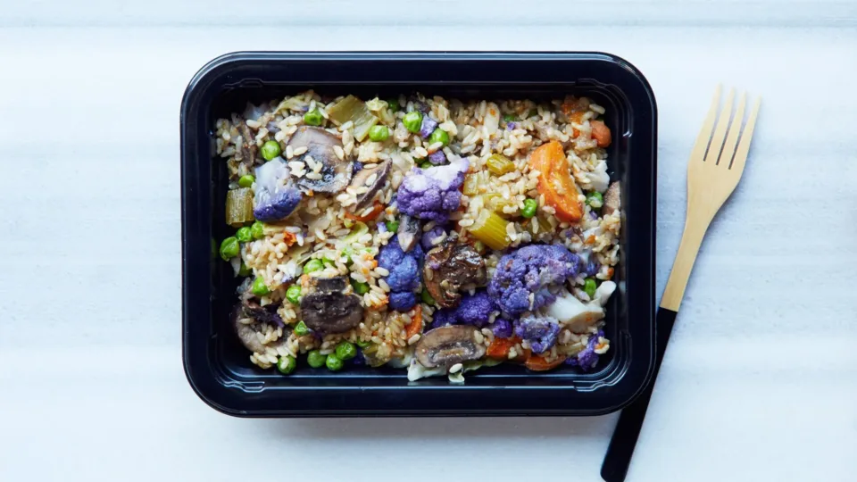 Prepared grain and vegetable meal in a food container beside a fork