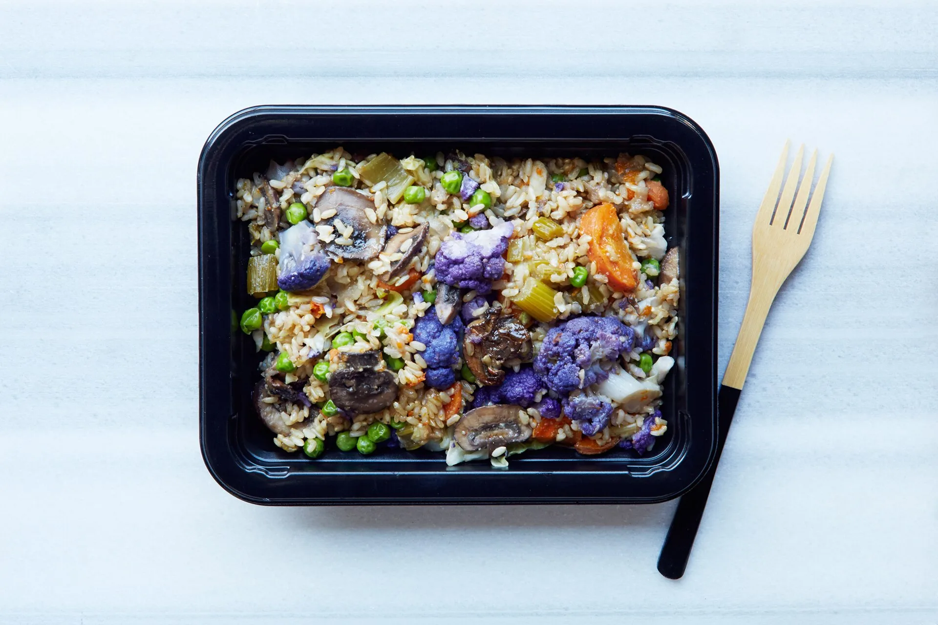 Prepared grain and vegetable meal in a food container beside a fork